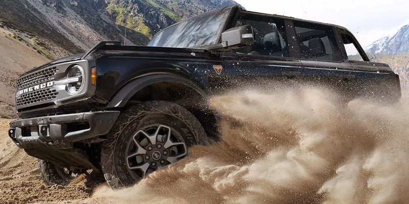 An off-road Ford Bronco splashes through desert and sand flying all around.